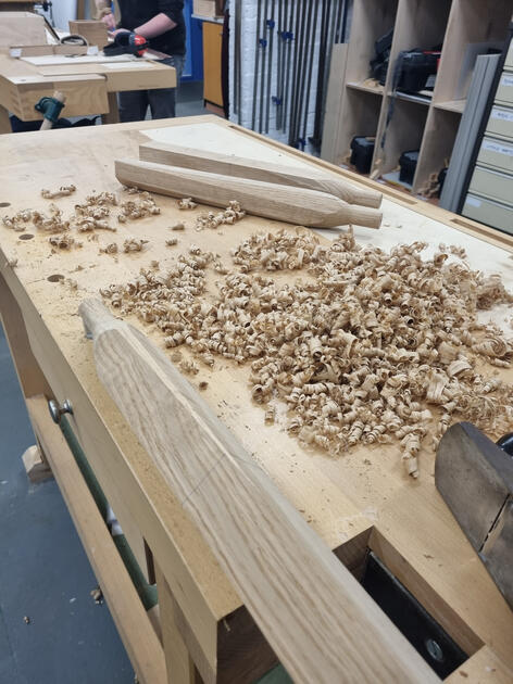 Hand planed stool legs with a pile of wood shavings.